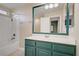 Bright bathroom featuring a tub/shower combo, large mirror and a vanity with a teal cabinet at 8005 Egypt Meadows Ave, Las Vegas, NV 89178