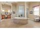 Luxurious bathroom featuring a stone-tiled jacuzzi tub, vanity area, and frosted glass block window accent at 670 Du Fort Ave, Henderson, NV 89002