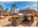 Backyard outdoor kitchen featuring a built-in grill, stone surround, and shaded tiki hut for relaxed outdoor dining at 790 Tossa De Mar Ave, Henderson, NV 89002