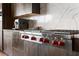 Close up of kitchen cooktop with stainless steel appliances, custom cabinets, marble backsplash, and red knobs at 1786 Diamond Rim Ct, Henderson, NV 89012