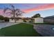 Rear exterior with covered patio, manicured lawn, and mature tree under vibrant sunset at 616 Lacy Ln, Las Vegas, NV 89107