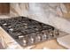 Close up of stainless steel cooktop with black grates and marble counter tops and back splash at 74 Innisbrook Ave, Las Vegas, NV 89113