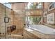 Luxurious bathroom featuring a glass-enclosed shower, soaking tub, and travertine tile surround at 2107 Eaglepath Cir, Henderson, NV 89074