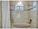 Clean bathroom featuring a shower-tub combo, neutral tiles, and a arched window at 2107 Eaglepath Cir, Henderson, NV 89074