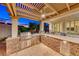 Outdoor kitchen with built-in barbecue, bar seating, pergola, travertine tile and exterior shutters at 2239 Discovery Lake Ct, Henderson, NV 89044