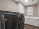 Modern laundry room with front loading machines, sink, white cabinets and window at 2153 Havensight Ln, Henderson, NV 89052