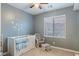 Comfortable Bedroom with gray walls, a ceiling fan, and a white crib with a blue striped blanket at 12382 Piazzo St, Las Vegas, NV 89141