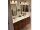 Dual vanity bathroom featuring warm wood cabinets, bright lighting, and decorative mirrors at 3999 Delos Dr, Las Vegas, NV 89103