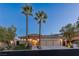 Charming front exterior featuring a stone archway, three-car garage, and mature palm trees lining the driveway at 11473 Glowing Sunset Ln, Las Vegas, NV 89135
