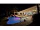 Backyard pool area with illuminated pool, grotto feature, lush tropical plants, and patio seating at 8290 Gagnier Blvd, Las Vegas, NV 89113