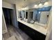 Bathroom with dual sinks, granite countertops, wood-look flooring, and a large framed mirror at 7068 Parrot Bay Way, Las Vegas, NV 89118