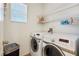 Well-lit laundry room featuring modern white washer and dryer set with overhead wire shelving for easy storage at 6121 Sinatra Sands Ct, Las Vegas, NV 89130