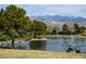 Picturesque pond view with lush green trees and mountains in the background, a serene escape with golf cart on the banks at 4571 S Via Roma Dr, Pahrump, NV 89061