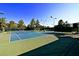 Well-maintained tennis court with a blue surface, complete with nets, lights, and surrounded by greenery at 71 Fountainhead Cir, Henderson, NV 89052
