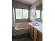 A well-lit bathroom featuring a soaking tub, oak vanity, and large windows at 5830 Springmist St, North Las Vegas, NV 89031