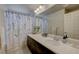Elegant bathroom features a long vanity with dark cabinets, large mirror, and shower with patterned curtain at 9835 Fox Estate St, Las Vegas, NV 89141