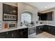 Well-equipped kitchen featuring stainless steel appliances, dark cabinetry, a large arched window, and mosaic backsplash at 9835 Fox Estate St, Las Vegas, NV 89141