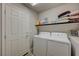 Convenient laundry room features modern washer and dryer, shelving for storage and a white painted door at 9835 Fox Estate St, Las Vegas, NV 89141