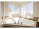 Close-up of a luxurious soaking tub with tile surround and large windows offering scenic views at 9257 Harbor Stream Ave, Las Vegas, NV 89149