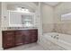 Bright bathroom featuring dark wood cabinets, double vanity, and large soaking tub with decorative tile surround at 16 Via Visione # 101, Henderson, NV 89011