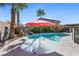 Inviting backyard pool featuring a baja shelf, rock waterfall, lush landscaping, and a vibrant red umbrella for relaxation at 746 Royal Course Ct, Las Vegas, NV 89148