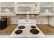 Close-up of white electric range, microwave, and speckled granite countertops, with decorative tile accents on the backsplash at 30 Strada Di Villaggio # 143, Henderson, NV 89011