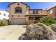 Two-story tan home with a concrete driveway, desert landscaping, and a covered front porch entry at 774 Wigan Pier Dr, Henderson, NV 89002
