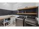 Modern laundry room featuring a front-loading washer and dryer, a wooden countertop, open shelves, and tiled walls at 6021 Vista Clara St, Las Vegas, NV 89148