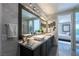 Bathroom featuring dual sinks, a large mirror with vanity lighting, and view into the Primary bedroom at 10605 Harvest Green Way, Las Vegas, NV 89135