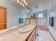 Well-lit bathroom with dual sinks, light blue walls, tile flooring, and a pink bathtub at 241 E Country Club Dr, Henderson, NV 89015