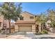 Two-story home with tan stucco, arched entryway, attached two-car garage, and desert landscaping at 2653 Rimbaud St, Henderson, NV 89044