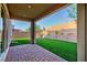 A covered patio with brick flooring overlooks the manicured artificial turf, xeriscaping, and block wall in the backyard at 26 Lilla Rosa St, Henderson, NV 89011