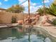 Custom pool area with a rock waterfall and slide, surrounded by lush landscaping and mature palm trees at 8970 Lansberry Ct, Las Vegas, NV 89147