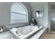 Close-up of soaking tub with arched window, marble surround, and decorative plants at 9325 Verlaine Ct, Las Vegas, NV 89145