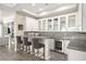 Bar area boasts white cabinets, glass shelves, grey countertop, mini-fridge, backsplash, and three stools at 12217 Tempestad Ave, Las Vegas, NV 89138