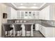 A stylish home bar featuring white cabinetry, glass shelving, mosaic backsplash and seating for three at 12217 Tempestad Ave, Las Vegas, NV 89138