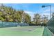 Outdoor tennis court with green surface and net, featuring lighting for evening play and surrounded by mature trees at 5421 Painted Mirage Rd, Las Vegas, NV 89149