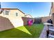 A fenced backyard featuring artificial turf, a basketball hoop, patio set, a grill and play equipment at 10922 Cambridge Lakes Ave, Las Vegas, NV 89166