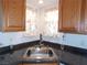 Close-up of a kitchen sink with wood cabinets, granite countertop, and floral window curtains at 710 Strawberry Pl, Henderson, NV 89002