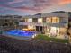 Backyard of modern home featuring a stunning pool with lounge chairs, outdoor seating, and mountain views at dusk at 801 Dragons Eye Dr, Henderson, NV 89012