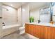 Modern bathroom featuring a sleek vanity, large mirror, soaking tub and neutral colored tile at 801 Dragons Eye Dr, Henderson, NV 89012