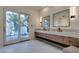 Bright bathroom with a double vanity, modern mirrors, and a sliding glass door to an outdoor patio at 10313 Orkiney Dr, Las Vegas, NV 89144