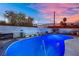 Backyard pool illuminated with vibrant light, complemented by seating and a backdrop of cityscape at dusk at 1805 Ivanhoe Way, Las Vegas, NV 89102