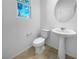 Well-lit powder room featuring a pedestal sink, toilet and a window providing natural light at 7059 Mackenzie Bay Ave, Las Vegas, NV 89179