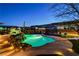 Backyard oasis featuring a stunning pool with a rock waterfall, ambient lighting, and covered lounge area at twilight at 6689 Sparks Ave, Las Vegas, NV 89142