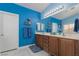 Bright blue bathroom featuring dual sinks, a large mirror, and oak cabinets, accented with soft blue rugs at 8213 Cabin Springs Ave, Las Vegas, NV 89131