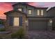 Dusk view of a two-story home showcasing a stone exterior, brown shutters, and a two-car garage at 8125 Skye Vineyard Dr, Las Vegas, NV 89166