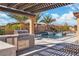 Outdoor kitchen and pool featuring bar seating, stainless grill, lounge seating and tiled waterfall at 9091 Becket Ranch Ct, Las Vegas, NV 89113