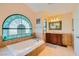 Bathroom featuring a deep soaking tub under an arched window and a wood vanity at 9532 Cliff View Way, Las Vegas, NV 89117