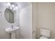 Clean half-bathroom featuring a pedestal sink, round mirror, and a white toilet at 6856 Pipil St, Las Vegas, NV 89166